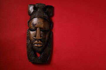 Antique African mask on a red background, top view, space for an inscription