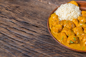 Chicken in curry cream sauce in a frying pan on a dark wooden background