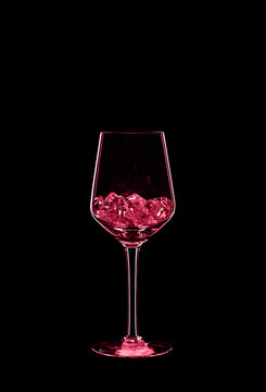 Wine glass filled with transparent crystals backlit and isolated on black background. Toned image in trendy magenta color of year 2023. Beverage glassware concept. Copy space.