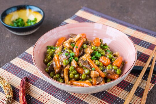 Asian style pork with mini carrots and green peas in a ceramic bowl on a brown concrete background. Wok dishes.