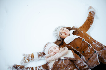 smiling modern mother and daughter making snow angel
