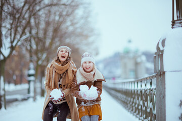 smiling stylish mother and daughter throwing snow