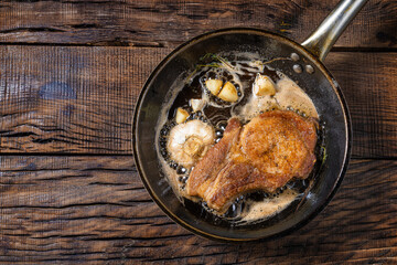 fried pork steak with seasonings in a frying pan, on a dark wooden background