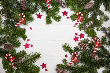 Fototapeta na wymiar Green Christmas tree branches with pinecones decorated with red stars and Christmas candy canes on a white wooden background top view