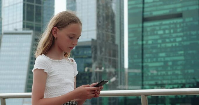 Blondy smiling cute teen girl is walking in city downtown browsing mobile phone. She is using navigator for her walk and watching on map at smartphone screen. Online life, internet addiction concept.