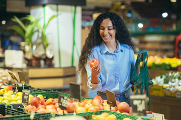 A beautiful young Hispanic woman is shopping in a supermarket. She stands smiling at the vegetable...