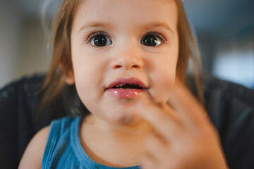 Close-up portrait of a young dirty baby girl eating in high chair. Healthy eating.