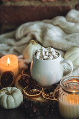 Fototapeta na wymiar Autumn cozy home composition with hot chocolate with marshmallow and candles. Aromatherapy on a grey fall morning, atmosphere of cosiness and relax. Wooden background, window sill, close up.
