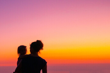 Silhouettes on a gradient sky. Mom and daughter are standing at sunset. Beautiful picture of motherhood