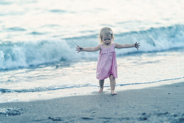 Little girl dancing on the shore. Perfect day at the sea. Toddler in a pink dress plays by the sea