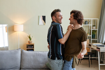 Side view portrait of carefree gay couple dancing in new home and laughing happily, copy space