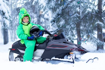 Fotobehang Boy sits in a green snowsuit holding a helmet on a snowmobile. © Saeedatun