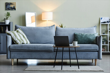 Background image of cozy blue-gray couch in minimal living room interior with laptop on coffee...