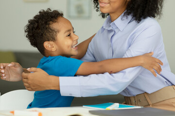 Happy african son hugging his mother on mother's day during the celebration. The boy hugs the teacher in the classroom.