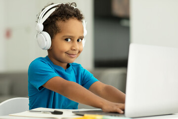 Smiling little African American boy studying with a laptop at home, cute schoolboy typing on a computer keyboard, doing homework