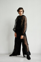 Full length portrait of non binary man wearing black chiffon outfit posing against white in fashion...