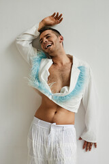 Vertical portrait of non binary man wearing cropped top and laughing carefree while posing against...