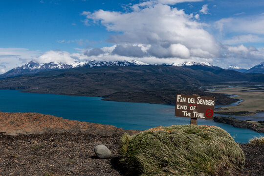 Sign stating end of the trail in Spanish and English with view of lake and mountains