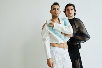 Portrait of two non binary young people wearing feminine outfits posing against white in fashion...