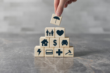The hand holds a wooden block with an umbrella putting it on top of other blocks with icons of...