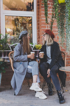 Young female best friends talking to each other discussing interesting themes during free time hipster girls joking and having fun together enjoying recreation with coffee to go on urban background