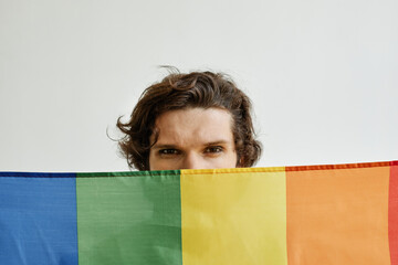 Minimal concept shot of young gay man holding pride flag, eyes visible looking at camera