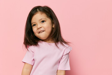 a cute little girl stands on a pink background in a pink T-shirt, cheerfully making faces at the camera waving her loose hair. The theme of fun and peace
