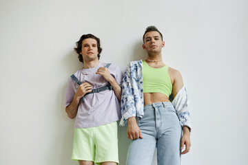 Portrait of two non binary men wearing pastel colored outfits with crop tops against white in...