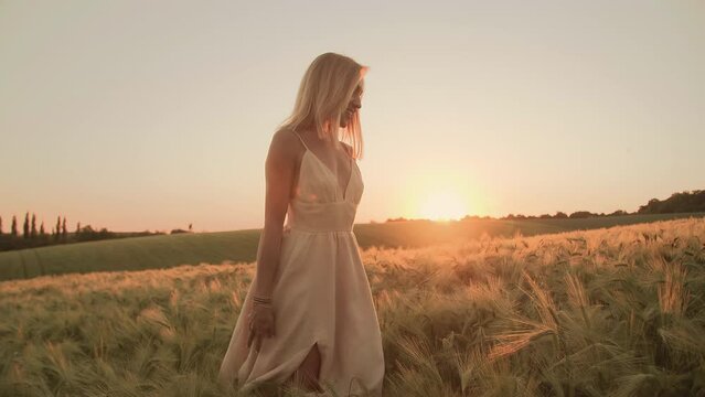 Young, blonde-haired woman touching wheat crops in the field. Close-up view of romantic, female tourist enjoying dreamy holiday around countryside landscape. High quality 4k footage
