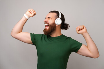 Handsome man wearing green t shirt enjoys music through wireless headphones over grey background in...