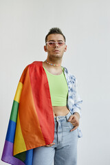 Vertical portrait of young gay man draped with pride flag against white background