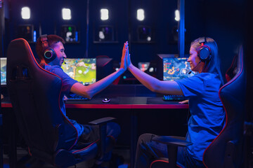 Professional players gamer rejoice in winning online video game, give each other five. Winner tournament esport, neon color back view, soft focus © Parilov
