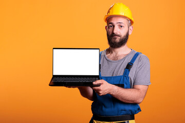 Happy craftsman expert showing laptop with white screen, holding pc with isolated copyspace display for advertisement in studio. Contractor worker using mockup template on computer.