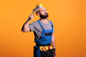 Craftsman decorator working on renovation with roller, painting walls with color and paintbrush. Construction worker holding rolling brush to do diy renovating project over studio background.