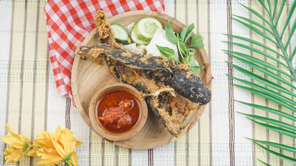 Fried catfish or “Pecel Lele” with fresh raw vegetables served on wooden plate. Indonesian food...