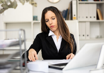 Woman bookkeeper sitting at desk in her workplace and doing her job.