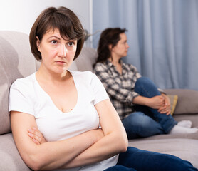 Portrait of sad mature female sitting at sofa after quarrel quarrel, woman on background