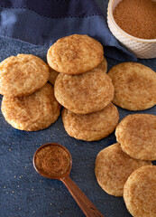 High angle view of homemade snickerdoodle cookies with a measuring spoon of sugar and cinnamon on a dark blue surface; copy space