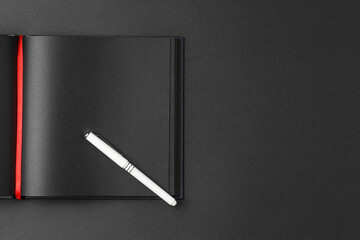 Black notebook on dark background with a white pen