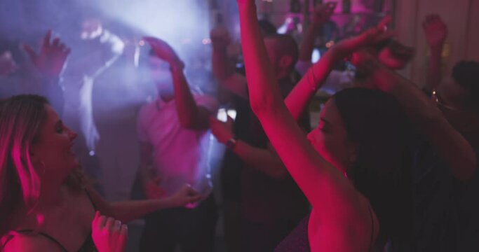 Night, party or friends at a disco to dance in celebration of new years at a social event with fun music. Excited, rave or happy women clubbing or dancing to celebrate happiness on dark dance floor