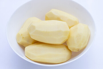 Raw peeled potatoes in white bowl on white background