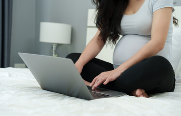 pregnant woman using laptop computer on bed