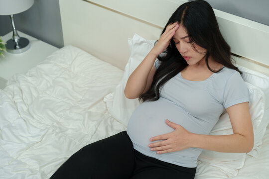 stressed pregnant woman suffering headache lying in bed - Powered by Adobe