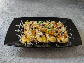 Grilled banana topped with grated cheese and chocolate chips. Served on black plate on grey textured background. Selective focus image.
