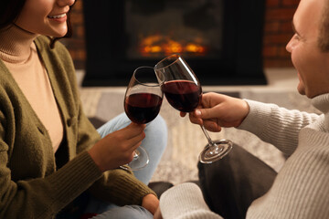 Happy lovely couple with glasses of wine spending time together near fireplace at home, closeup