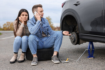 Young man calling to car service on roadside. Tire puncture