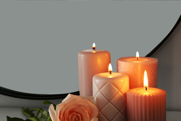 Fototapeta na wymiar Burning candles and rose near mirror in room, closeup. Space for text