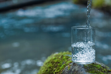 Fresh water pouring into glass on stone near river. Space for text