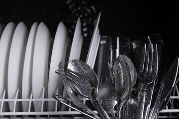 Clean wet plates and cutlery in dishwasher, closeup