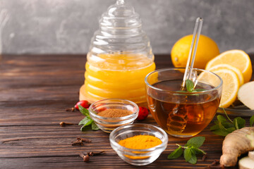 Tea with honey and ingredients on wooden table. Space for text